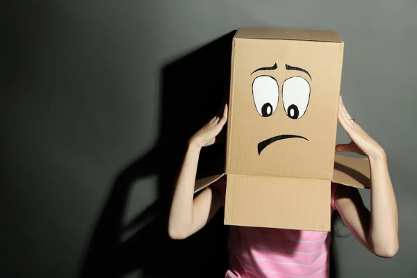 Donna con scatola di cartone in testa con viso triste, su sfondo grigio — Foto Stock