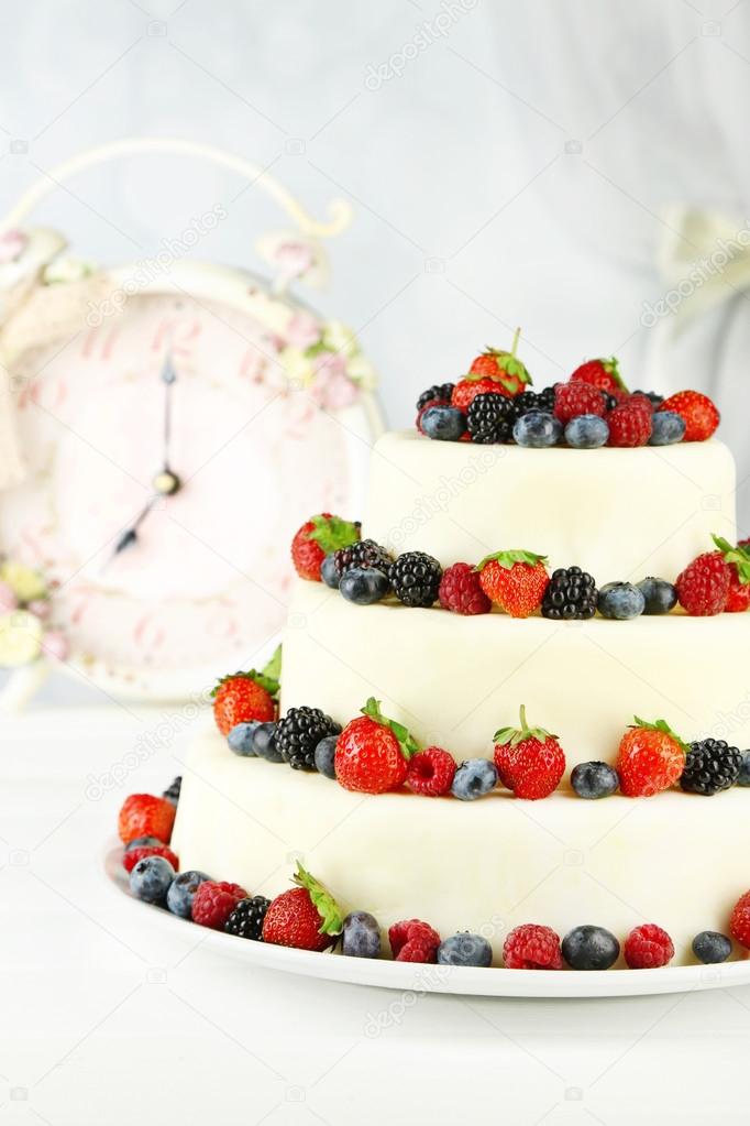 Beautiful wedding cake with berries on wooden table, on light background
