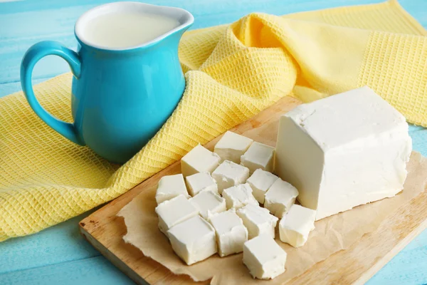 Fresh butter on cutting board and jug with milk, on color wooden background — Stock Photo, Image