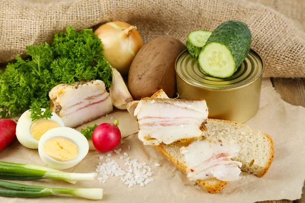 Bacon, fresh vegetables, boiled egg and bread on paper, on wooden background. Village breakfast concept. — Stock Photo, Image