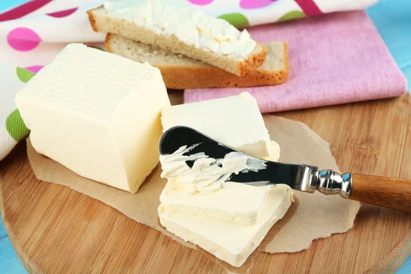 Mantequilla fresca y rebanadas de pan en la tabla de cortar, sobre fondo de madera de color — Foto de Stock