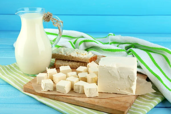 Manteiga fresca na tábua de corte e jarro com leite, na cor de fundo de madeira — Fotografia de Stock