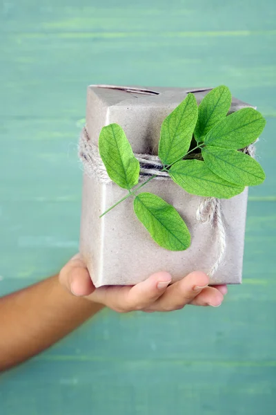 Female hand holding natural style handcrafted gift box with fresh leaves and rustic twine, on wooden background — Stock Photo, Image