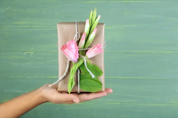 Main féminine tenant boîte cadeau artisanale de style naturel avec des fleurs fraîches et de la ficelle rustique, sur fond en bois — Photo