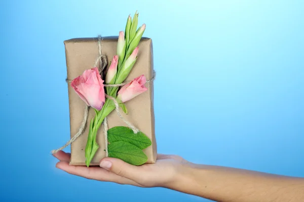 Female hand holding natural style handcrafted gift box with fresh flowers and rustic twine, on color background — Stock Photo, Image