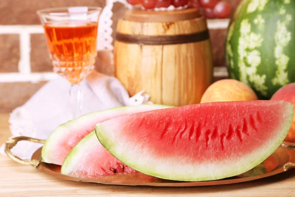 Composition de pastèque mûre, fruits, vin rose en verre et tonneau en bois sur table en bois de couleur, sur fond de briques — Photo