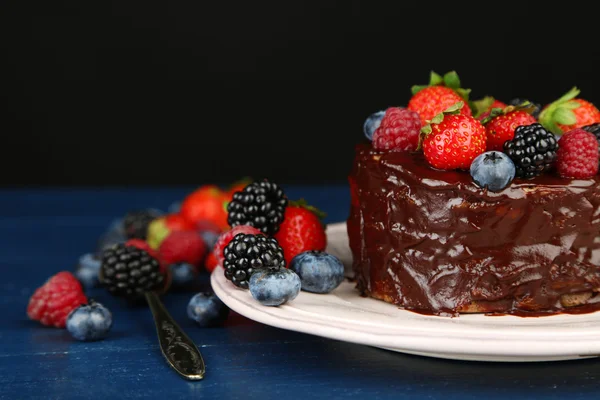 Tasty chocolate cake with different berries on wooden table, on dark background — Stock Photo, Image