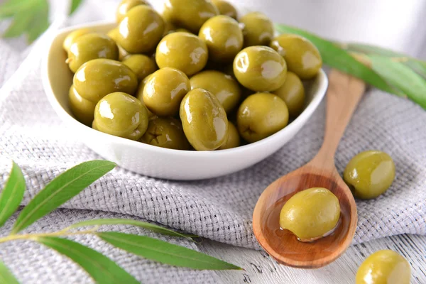 Зеленые оливки в миске с листьями на столе крупным планом — стоковое фото
