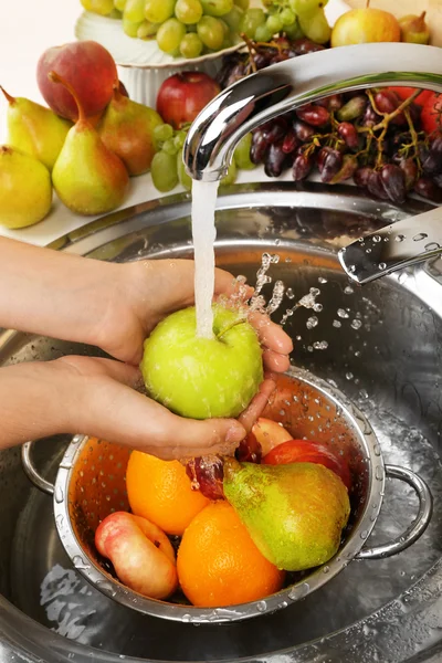 Woman's hands washing apple and other fruits in colander in sink — Stock Photo, Image