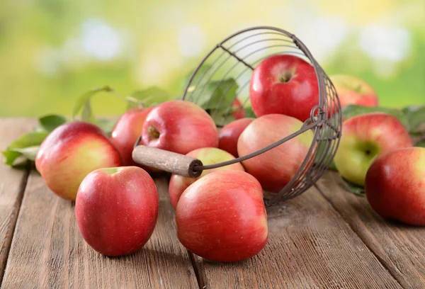 Manzanas dulces en canasta de mimbre sobre mesa sobre fondo brillante — Foto de Stock