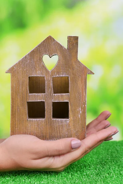 Woman hands holding small house on grass on bright background — Stock Photo, Image