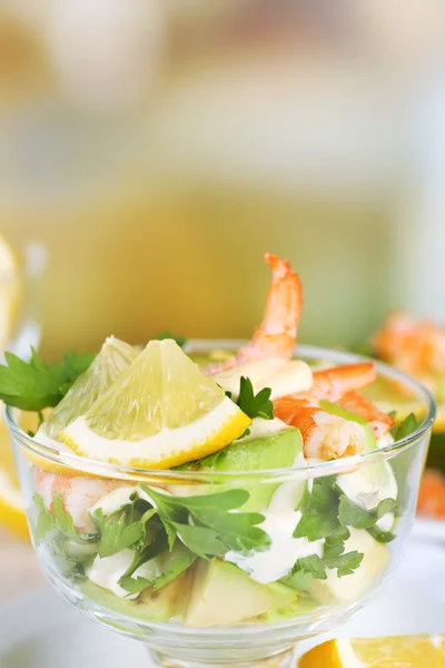 Gustose insalate con gamberetti e avocado in ciotola di vetro e su piatto, sul tavolo, su sfondo brillante — Foto Stock
