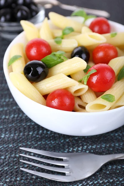 Nudeln mit Tomaten, Oliven und Basilikumblättern in einer Schüssel auf dunklem Stoff Hintergrund — Stockfoto