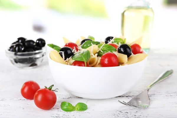 Nudeln mit Tomaten, Oliven und Basilikumblättern in einer Schüssel auf einem Holztisch vor natürlichem Hintergrund — Stockfoto