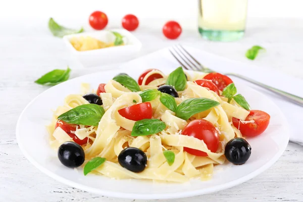 Spaghetti with tomatoes, olives and basil leaves on plate on wooden table — Stock Photo, Image