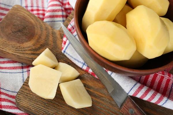 Batatas descascadas cruas na tigela na tábua de corte, no fundo de madeira — Fotografia de Stock