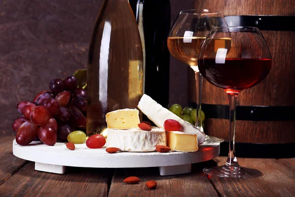 Abendessen bestehend aus Camembert-Käse, Wein und Trauben am Stand und Weinfass auf Holztisch auf braunem Hintergrund — Stockfoto