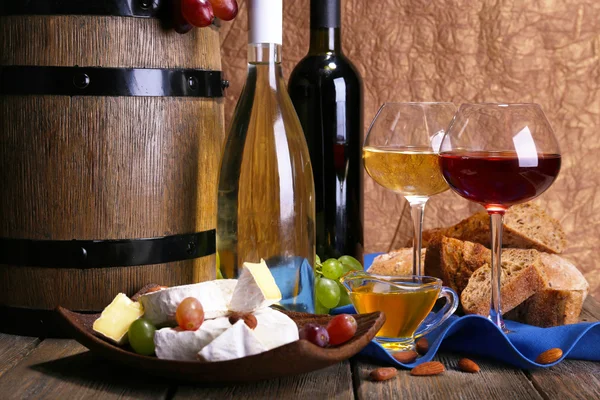 Abendessen bestehend aus Camembert und Brie-Käse, Honig, Wein und Trauben auf Serviette in Korb und Weinfass auf Holztisch auf braunem Hintergrund — Stockfoto