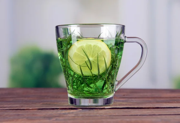 Glass of estragon drink with lemon on wooden table on bright background — Stock Photo, Image