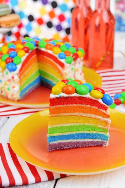 Köstlicher Regenbogenkuchen auf Teller auf Tisch vor hellem Hintergrund — Stockfoto