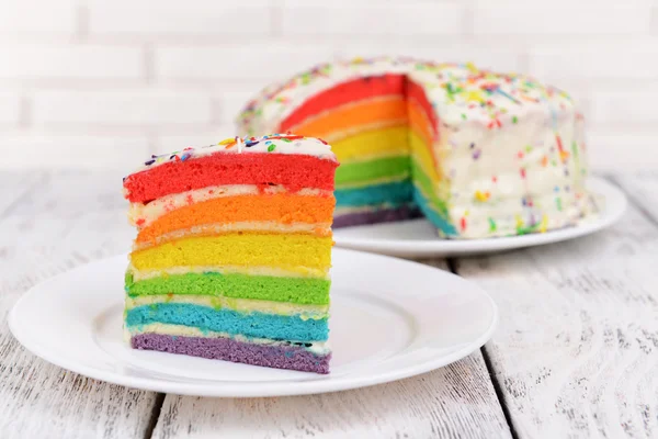 Delicioso pastel de arco iris en el plato en la mesa sobre fondo claro —  Fotos de Stock