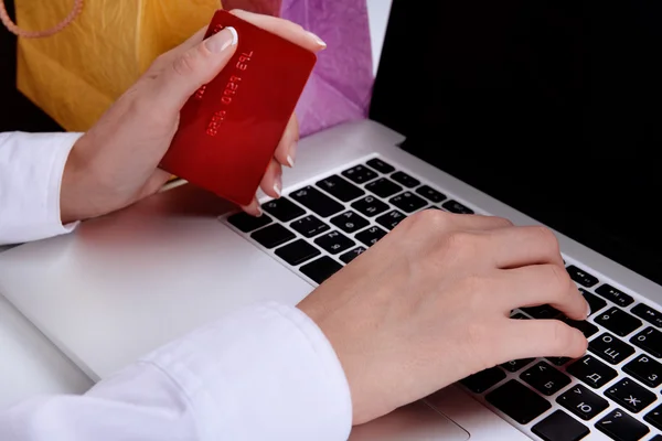 テーブルにノート パソコンと紙の袋でクレジット カードを保持している女性の手をクローズ アップ — ストック写真