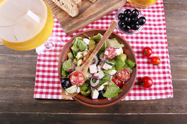 Kom van Griekse salade geserveerd met een glas wijn en brood op servet op houten achtergrond — Stockfoto