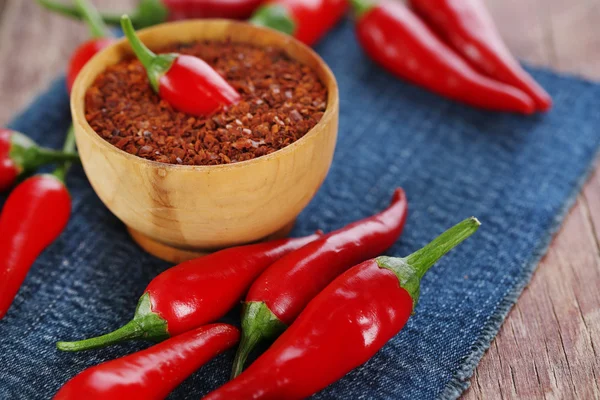 Red hot chili peppers and milled pepper in bowl on color fabric napkin, on wooden background — Stock Photo, Image