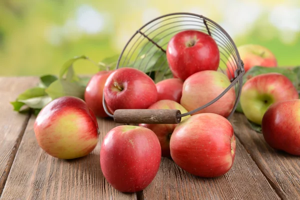 Söta äpplen i flätade korgen på bordet på ljus bakgrund — Stockfoto