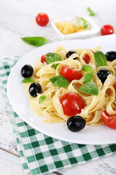 Spaghetti with tomatoes, olives and basil leaves on plate on napkin on wooden background — Stock Photo, Image