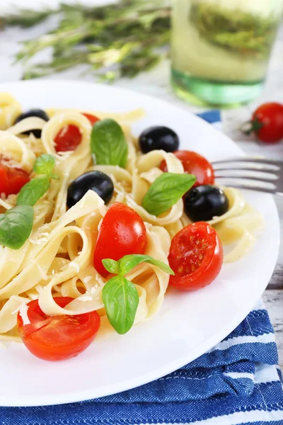 Espaguetis con tomates, aceitunas y hojas de albahaca en plato sobre servilleta sobre fondo de madera — Foto de Stock