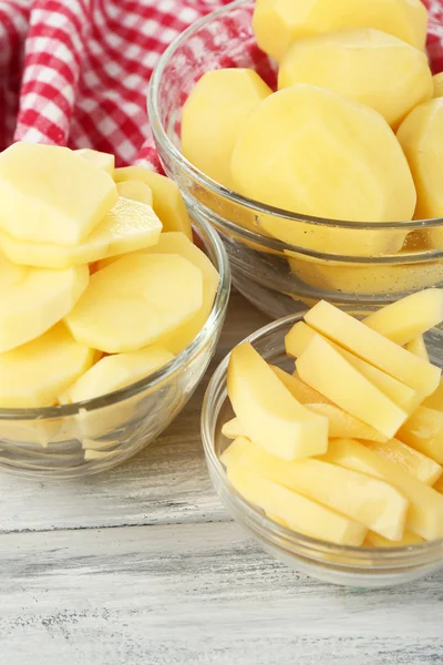 Rohe geschälte und in Scheiben geschnittene Kartoffeln in Glasschalen auf farbigem Holzhintergrund — Stockfoto