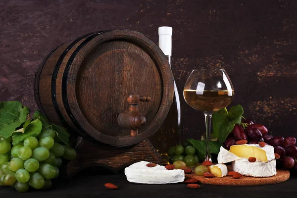 Ужин, состоящий из сыра Камамбер, вина и винограда на разделочной доске и бочки вина на деревянном столе на коричневом фоне — стоковое фото