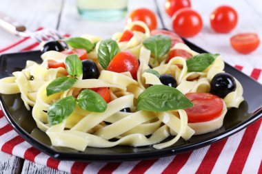 Ahşap masa peçeteye üzerinde siyah plaka üzerinde spagetti domates, zeytin ve fesleğen yaprakları