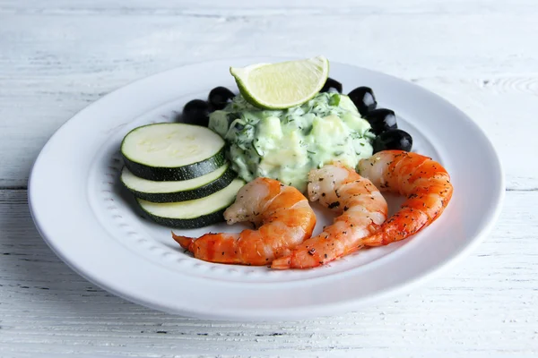 Crevettes fraîches avec avocat, olives, citron vert et salade dans une assiette ronde blanche sur fond de bois — Photo