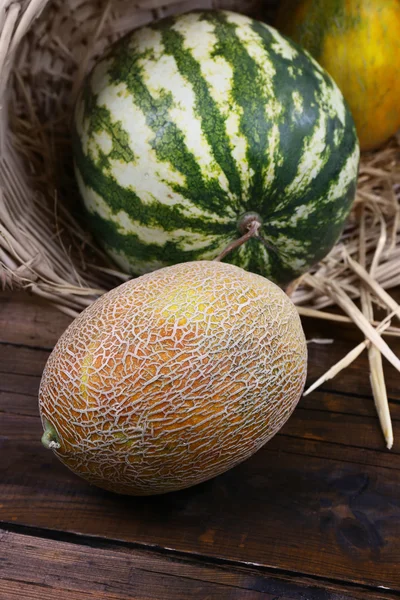 Melons and watermelon in wicker basket on wooden background — Stock Photo, Image