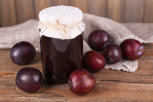 Tasty plum jam in jar and plums on wooden table close-up — Stock Photo, Image