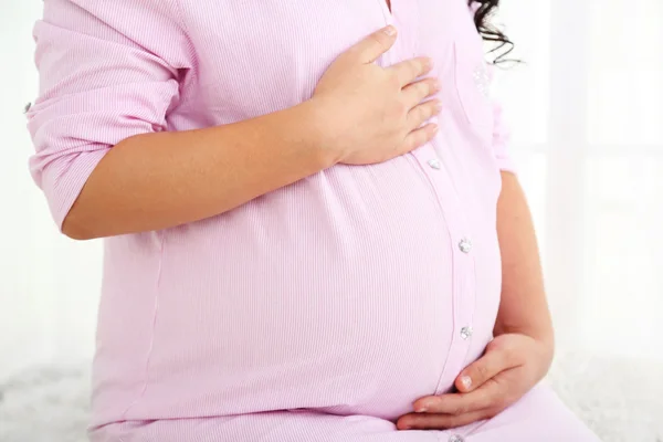 Jonge zwangere vrouw zitten op tapijt op lichte achtergrond — Stockfoto