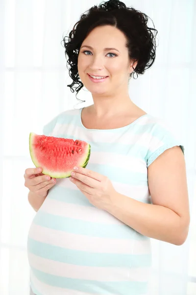 Young pregnant woman holding slice of watermelon on light background — Stock Photo, Image