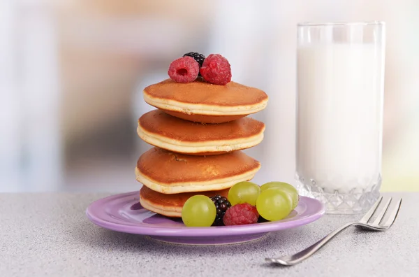 Pancake dengan buah beri dan segelas susu di atas meja dengan latar belakang cerah — Stok Foto
