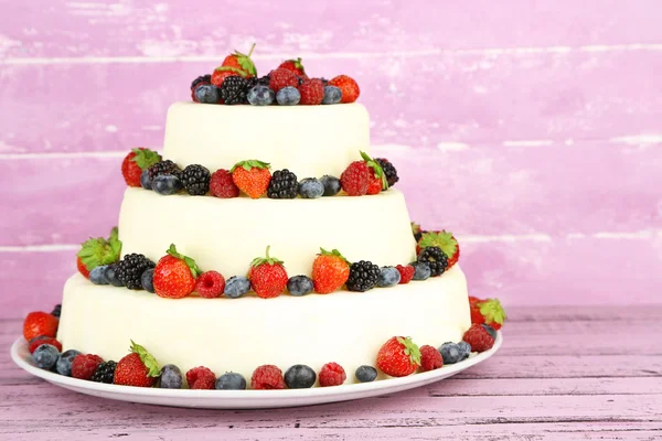 Beautiful wedding cake with berries on pink wooden background — Stock Photo, Image