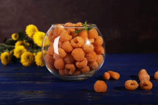 Himbeeren in Glas und Wildblumen auf dunkelblauem Holztisch vor dunklem Hintergrund — Stockfoto