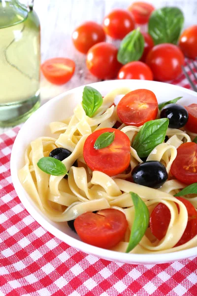 Špagety s rajčaty, olivami a bazalkou ponechává na štítku na pozadí tkaniny — Stock fotografie