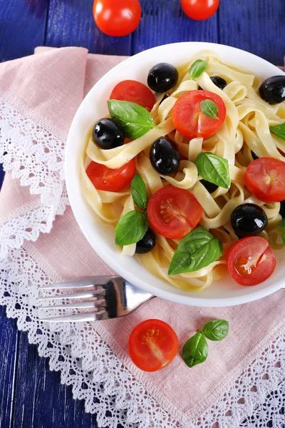 Spaghetti mit Tomaten, Oliven und Basilikumblättern auf Teller auf rosa Spitzenserviette auf Holzgrund — Stockfoto