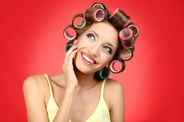 Menina bonita em encrespadores de cabelo no fundo vermelho — Fotografia de Stock
