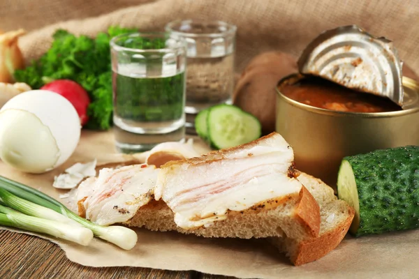 Tocino, verduras frescas, huevo cocido y pan sobre papel, vasos con vodka sobre fondo de madera. concepto de desayuno Village . — Foto de Stock