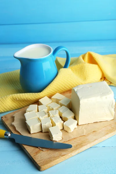 Frische Butter auf Schneidebrett und Krug mit Milch, auf farbigem Holzgrund — Stockfoto