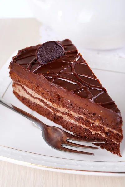 Pedazo de pastel de chocolate en el plato en la mesa de madera sobre fondo de tetera —  Fotos de Stock
