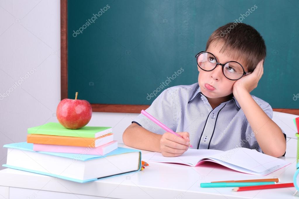 Schoolboy sitting in classroom on blackboard background Stock Photo by  ©belchonock 54197367
