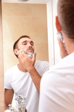 Genç adam banyoda sakalını kesiyor.